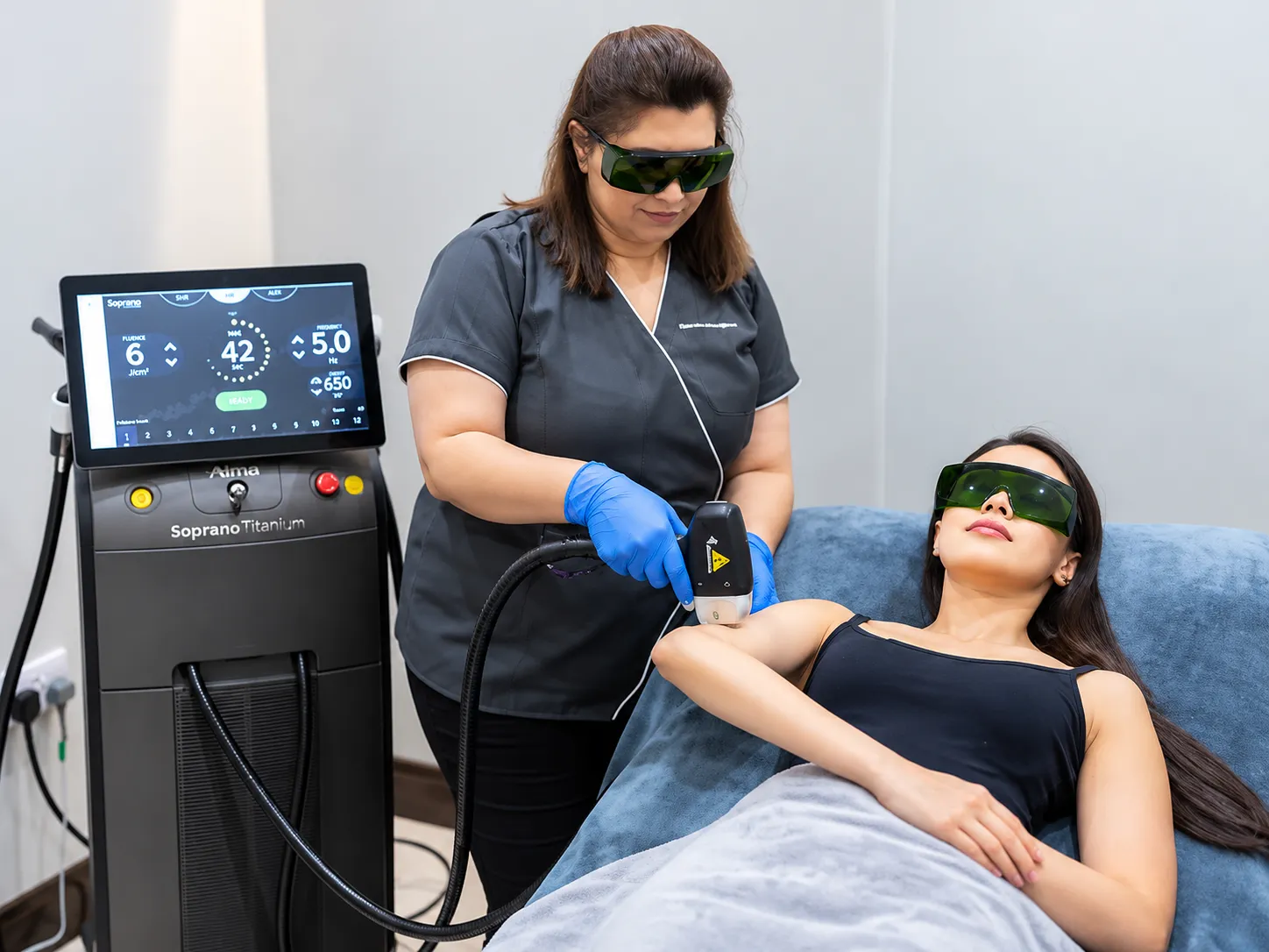 Therapist in gloves performing a laser hair removal session on a client wearing protective eyewear